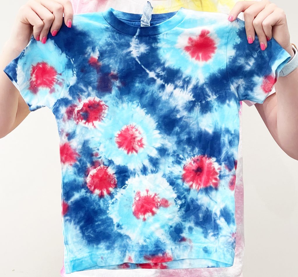 girl holding red white and blue fireworks sunburst tie dye shirt