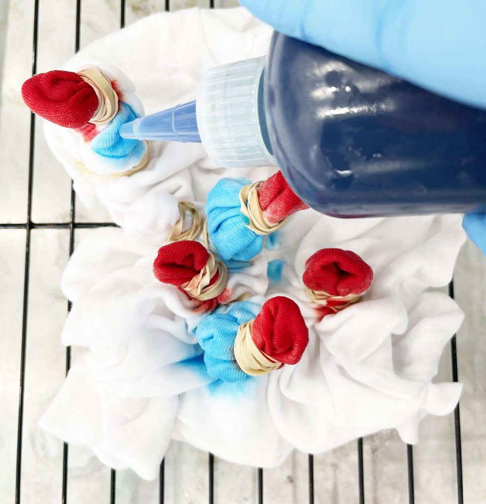 applying light blue dye to fireworks tie dye shirt with sunburst pattern