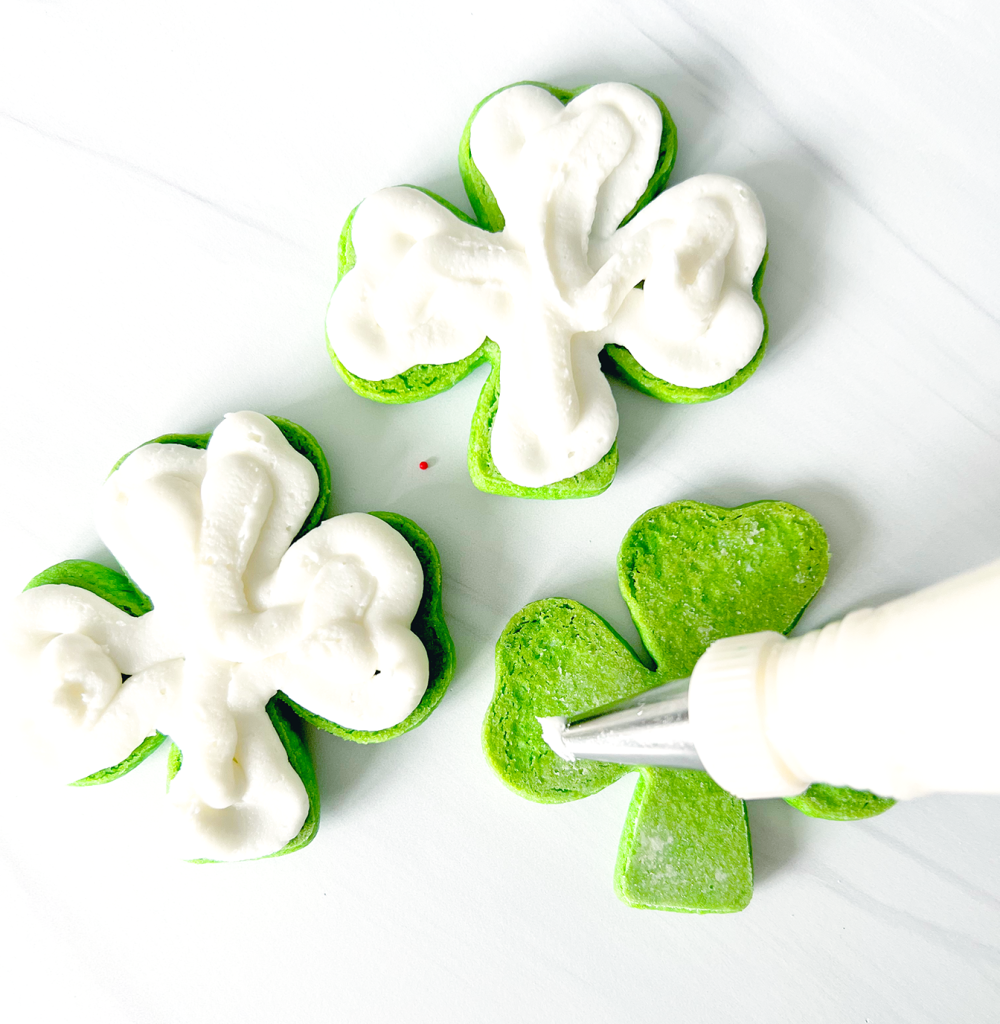 white icing being piped onto shamrock sugar cookies