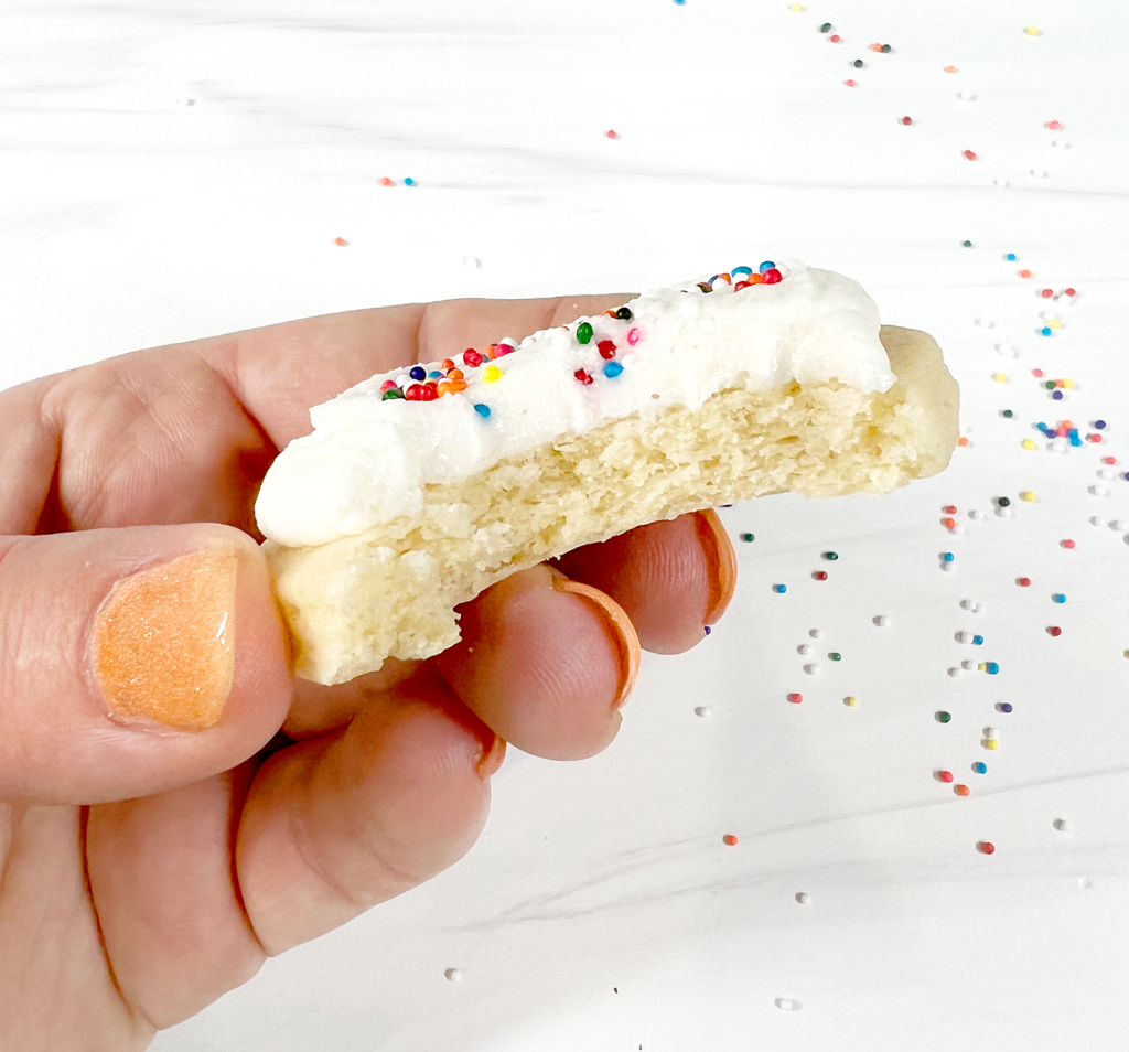 cut out sugar cookies with rainbow sprinkles with bite out close up and hand holding it