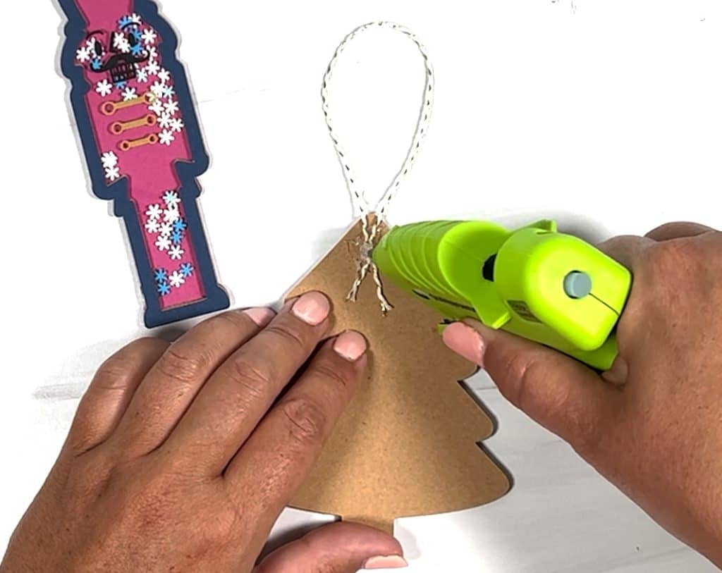 adding ribbon to back of diy shaker christmas ornament with hot glue gun