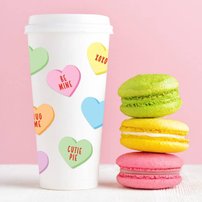 free printable conversation hearts stickers on white tumbler with a pink background and colorful macarons in the foreground