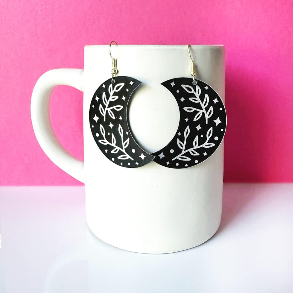 laser cut and engraved metal earrings hanging on white mug